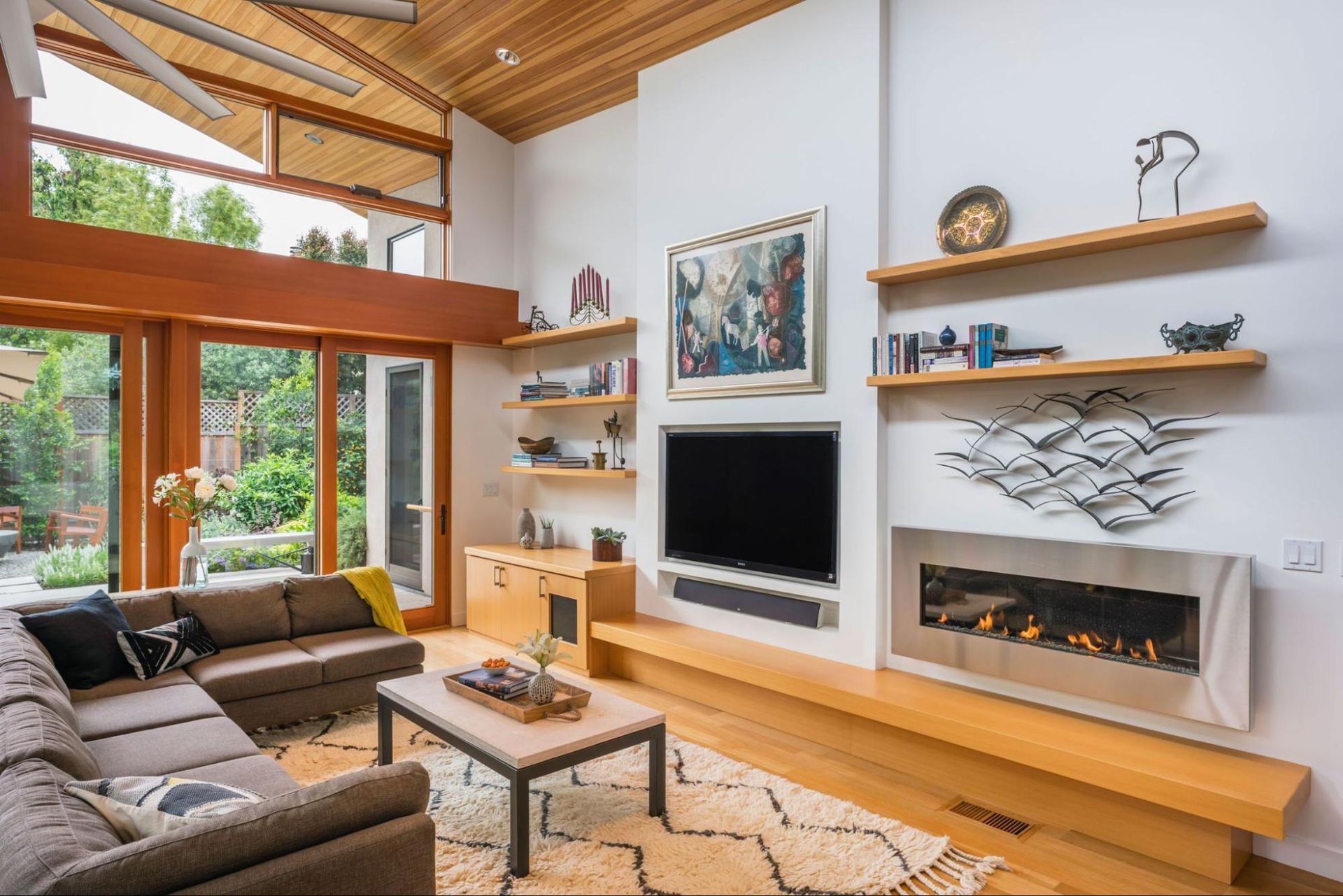 A built-in tv, fireplace with long hearth, and floating shelves anchor the living area