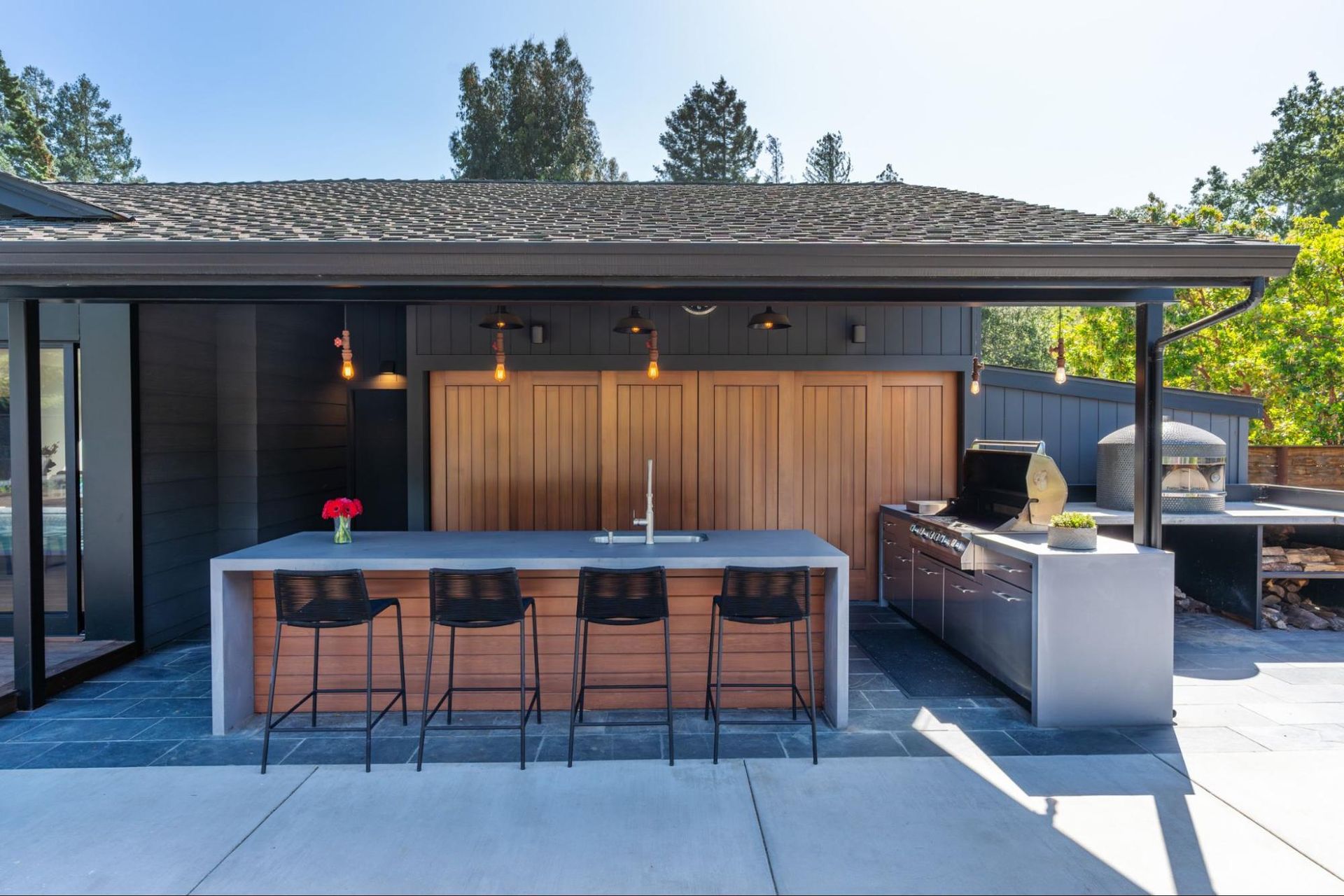 An outdoor kitchen with a large island below an existing roof overhang