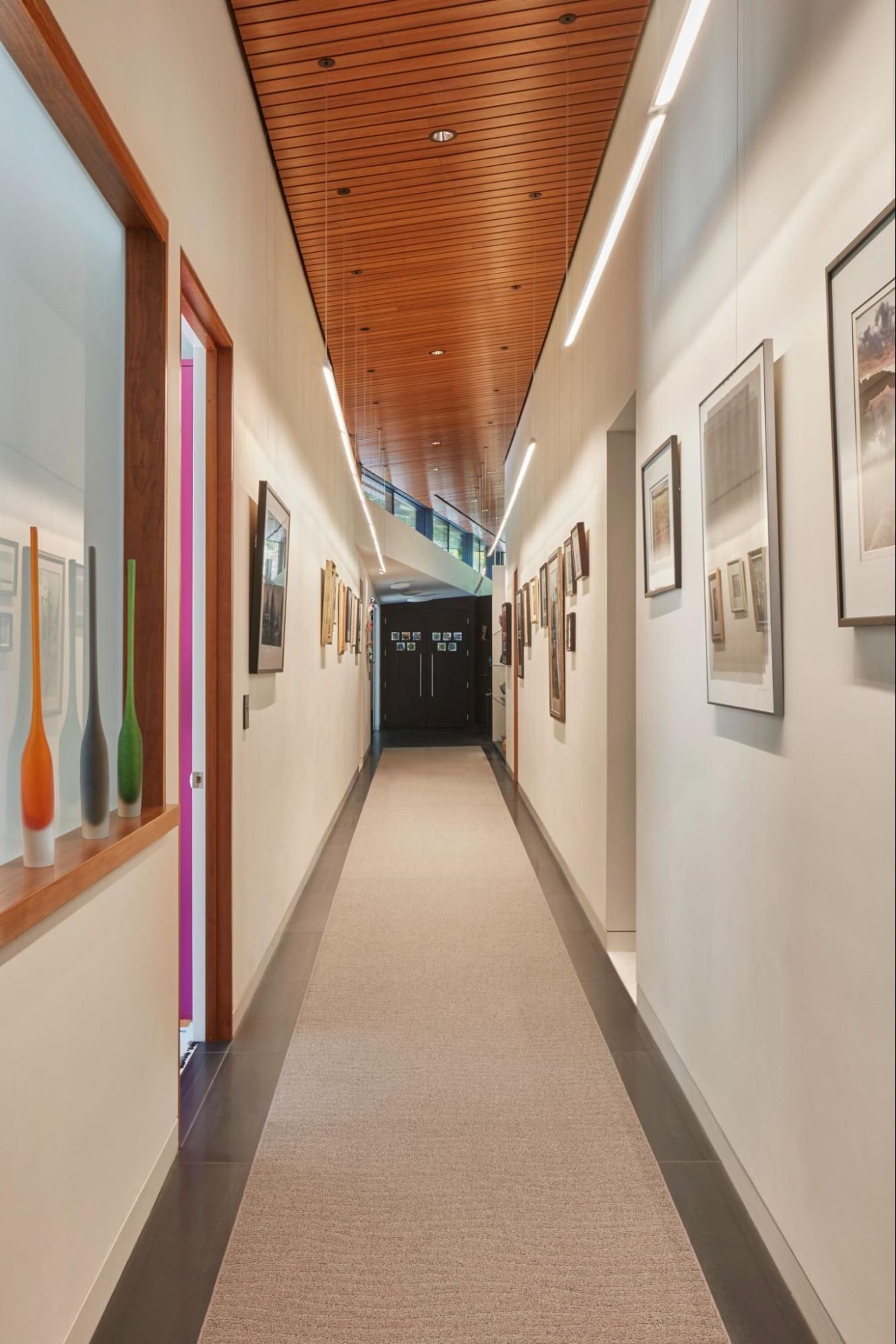 Long hallway with high windows and a wood ceiling displays art