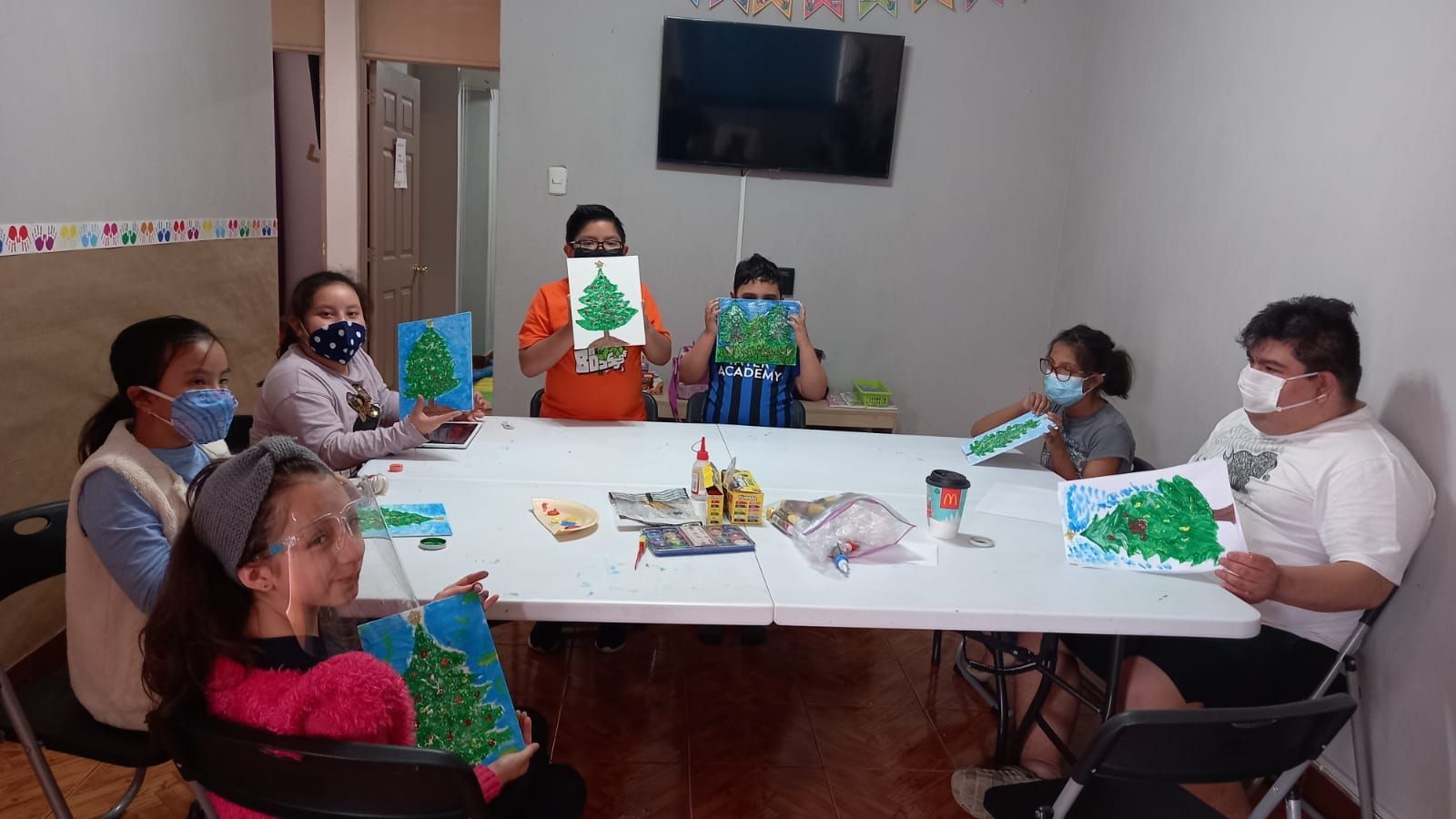 Un grupo de personas están sentadas alrededor de una mesa sosteniendo árboles de Navidad.
