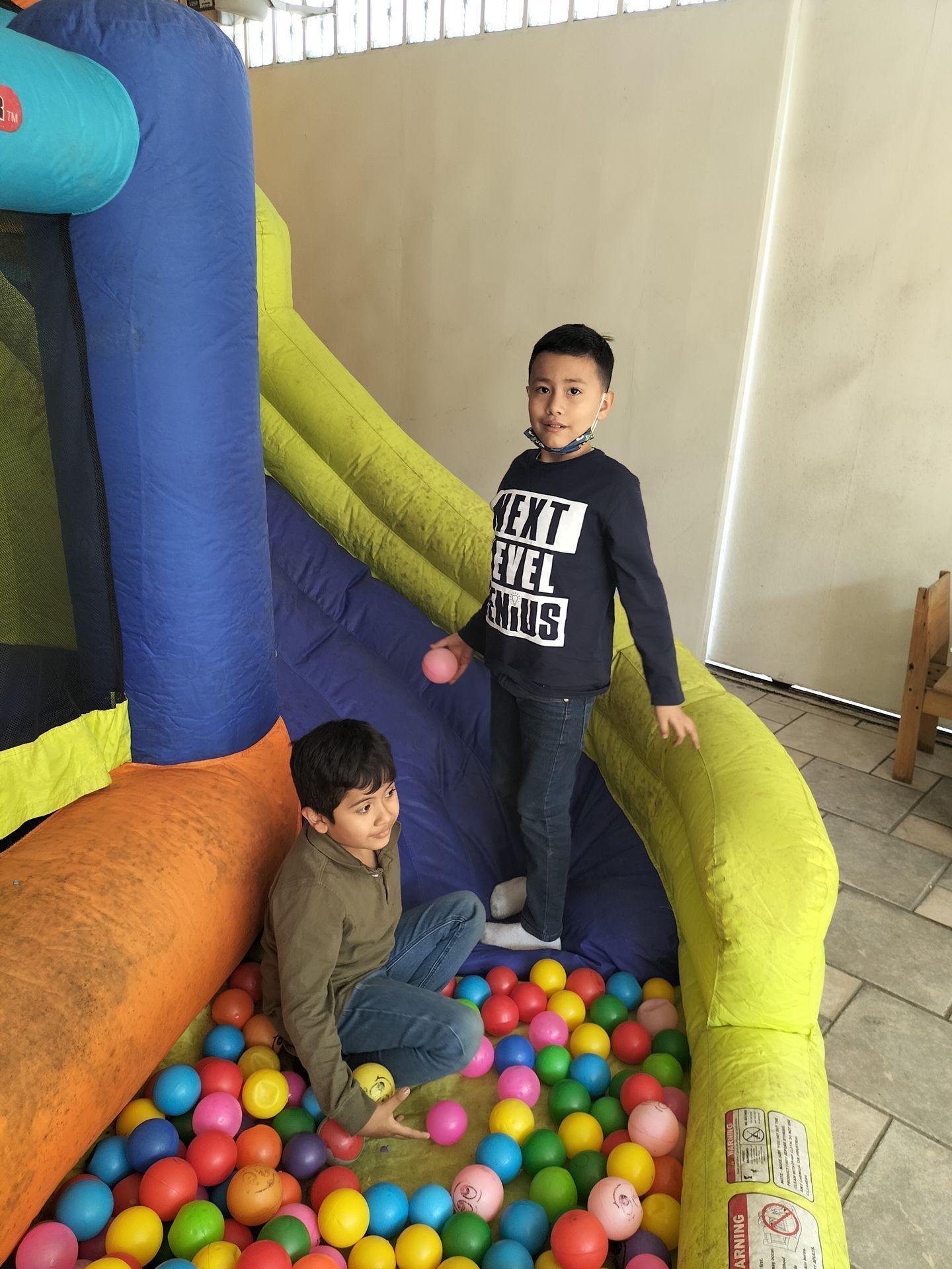 Dos niños están jugando en una piscina de pelotas al lado de un castillo inflable.