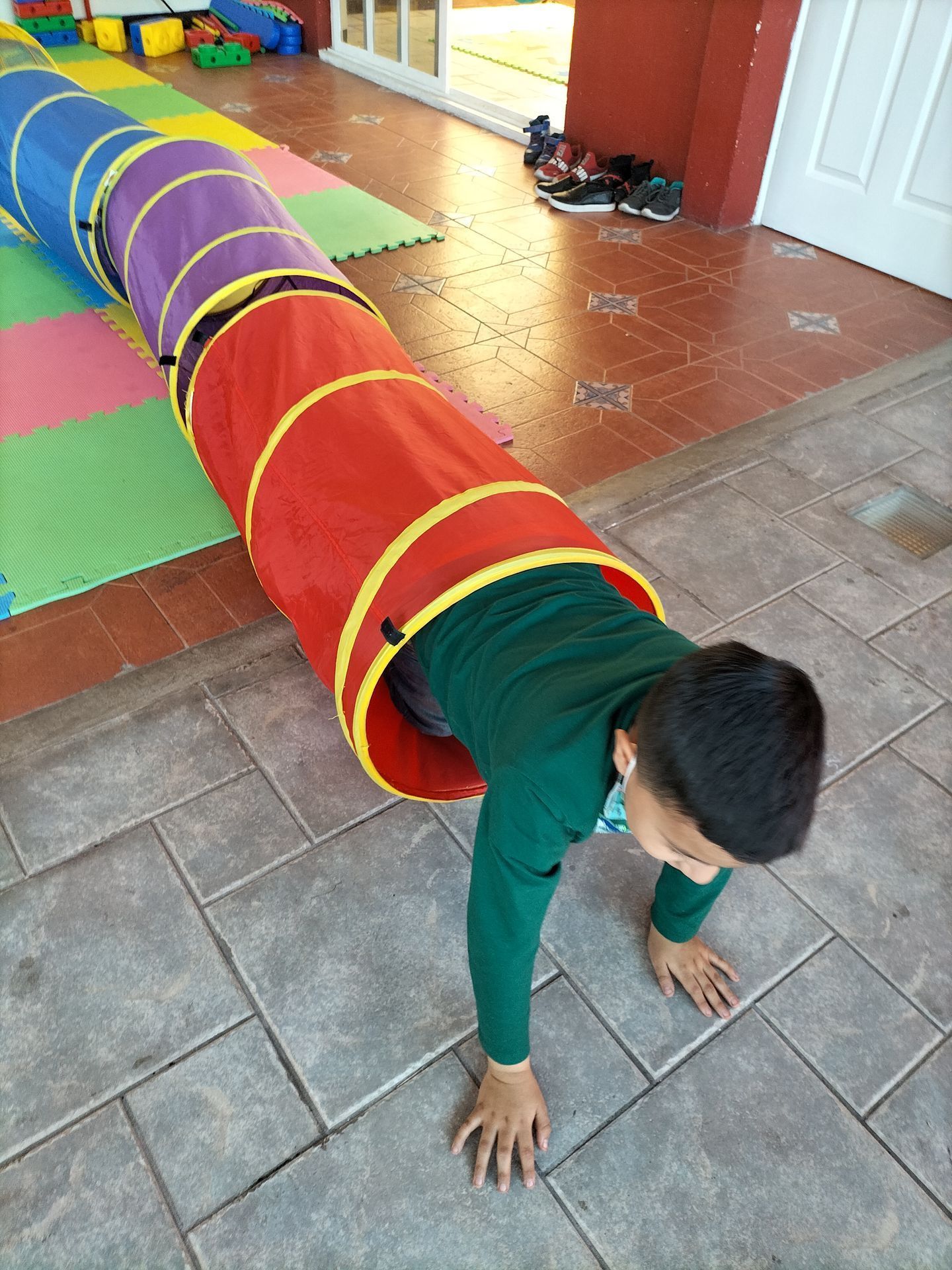 Un niño pequeño está haciendo flexiones en un túnel colorido.