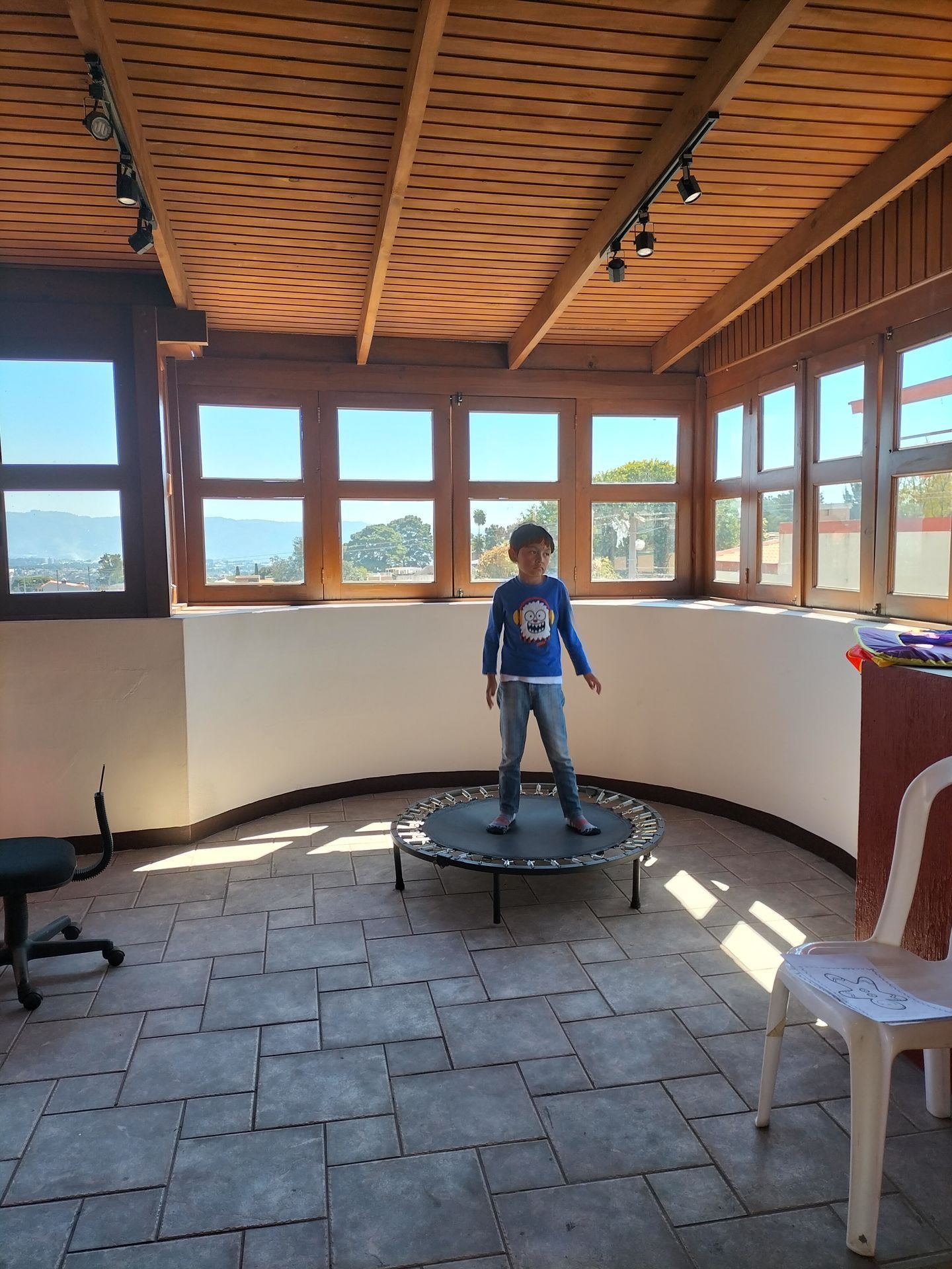 Un niño pequeño está parado en un trampolín en una habitación con muchas ventanas.