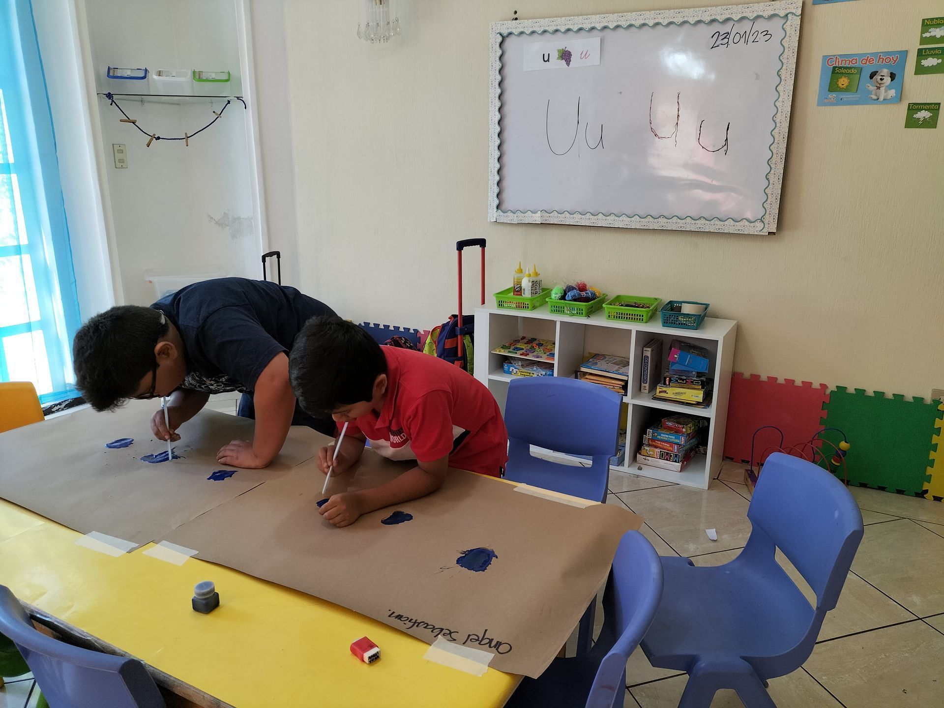 Dos niños están dibujando en un trozo de papel en un aula.