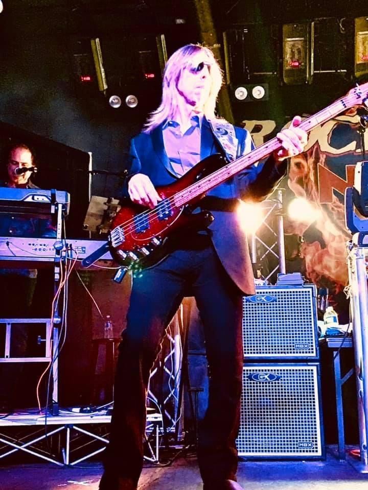 A man with long blonde hair is playing a bass guitar on stage