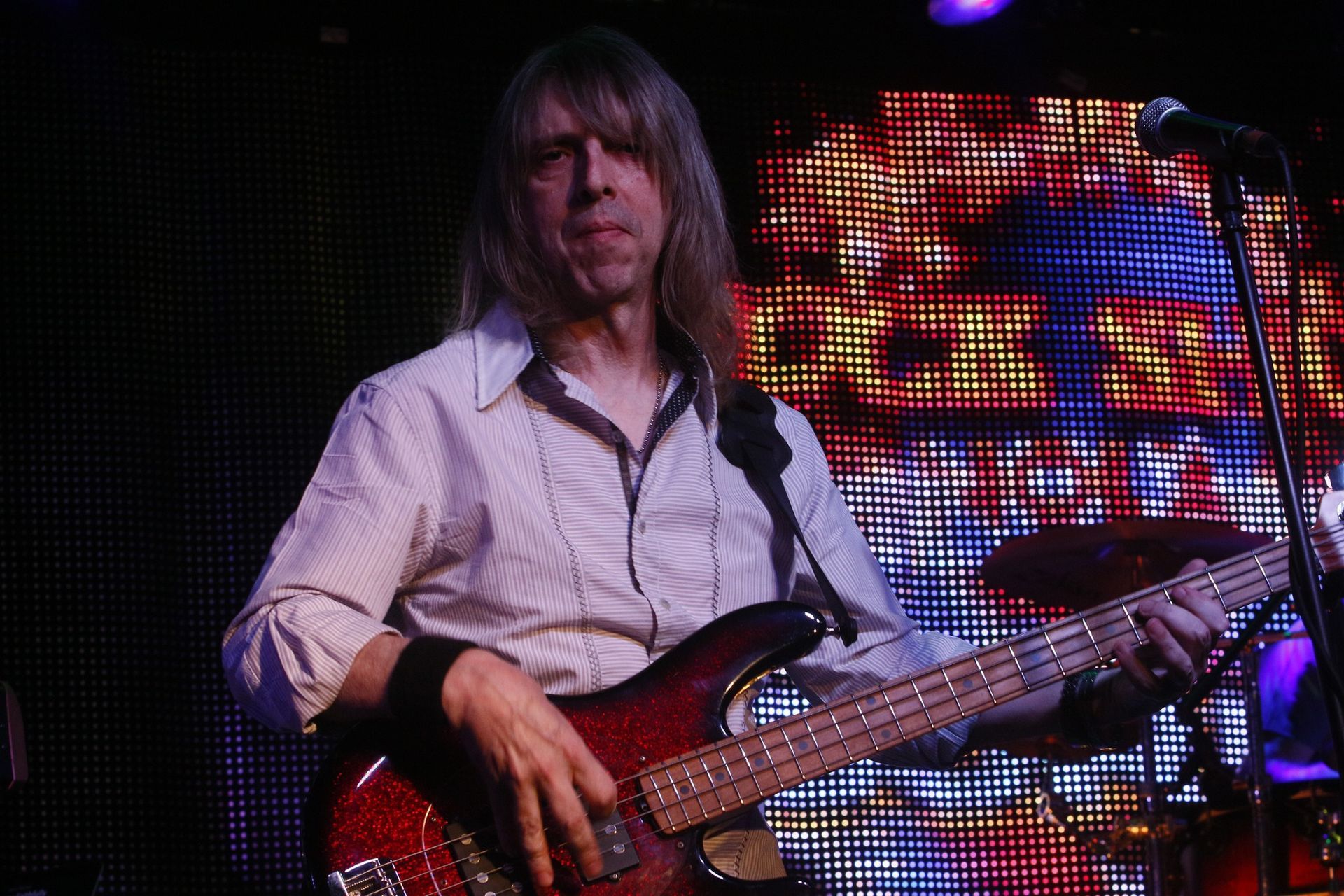 A man with long hair is playing a bass guitar on a stage.