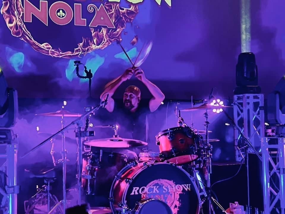 A man playing drums in front of a sign that says nola