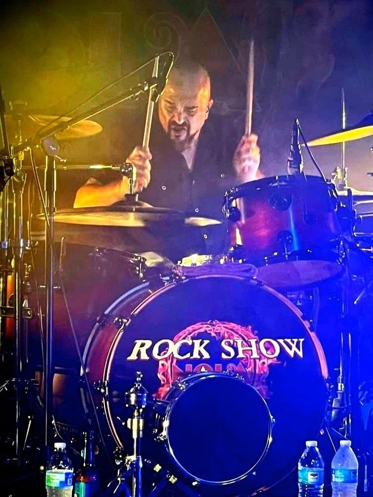 A man is playing drums in front of a drum that says rock show