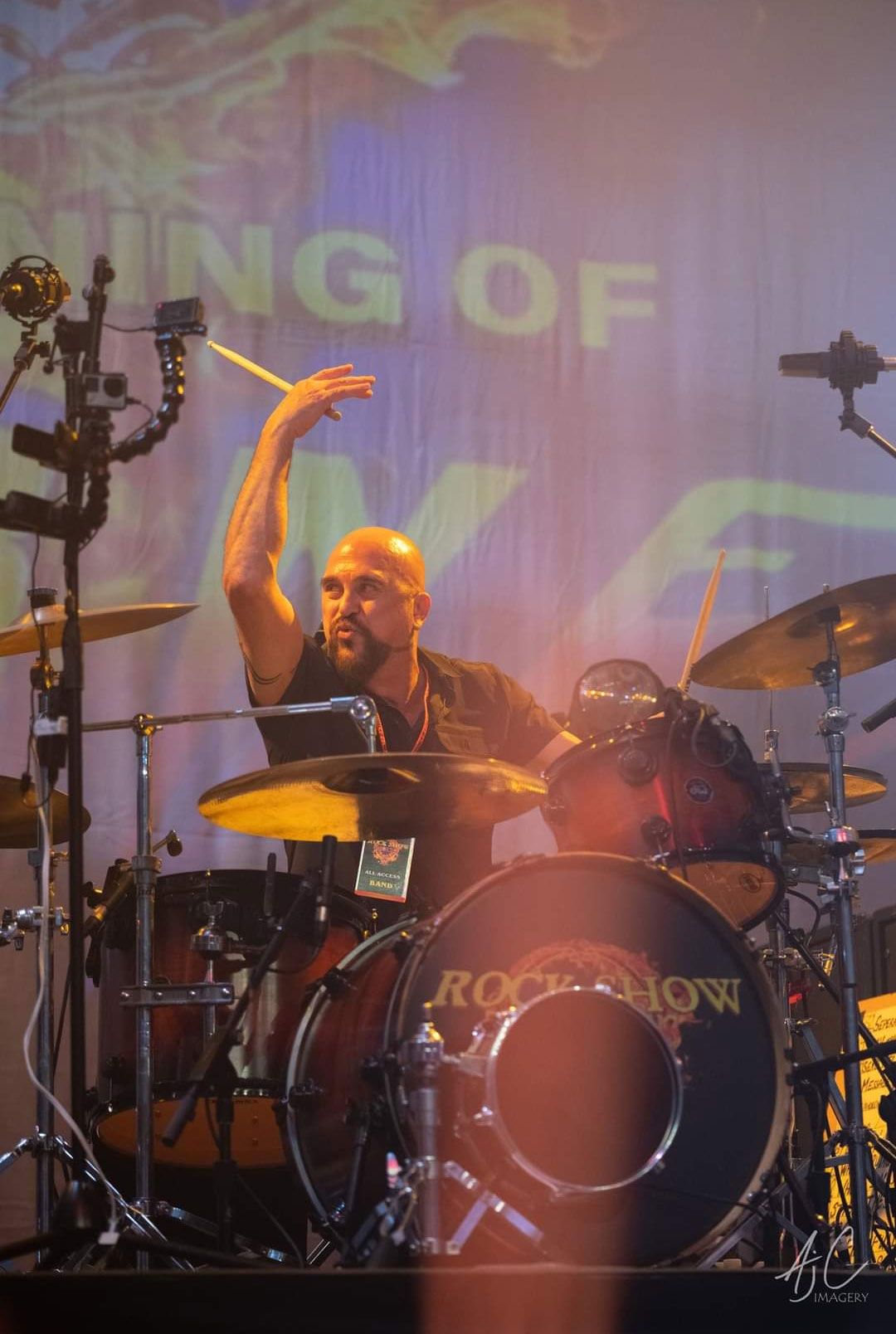 A man is playing drums on a stage in front of a large screen.