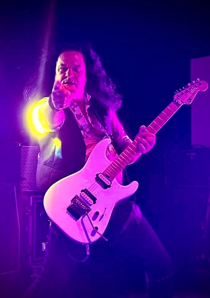 A man is playing a guitar in a dark room with purple lights.