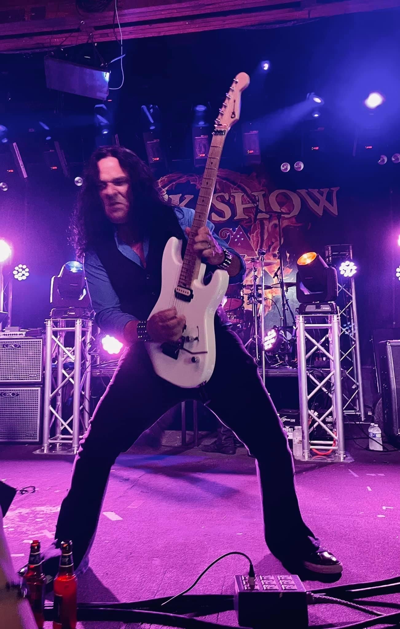 A man is playing a white electric guitar on a stage.