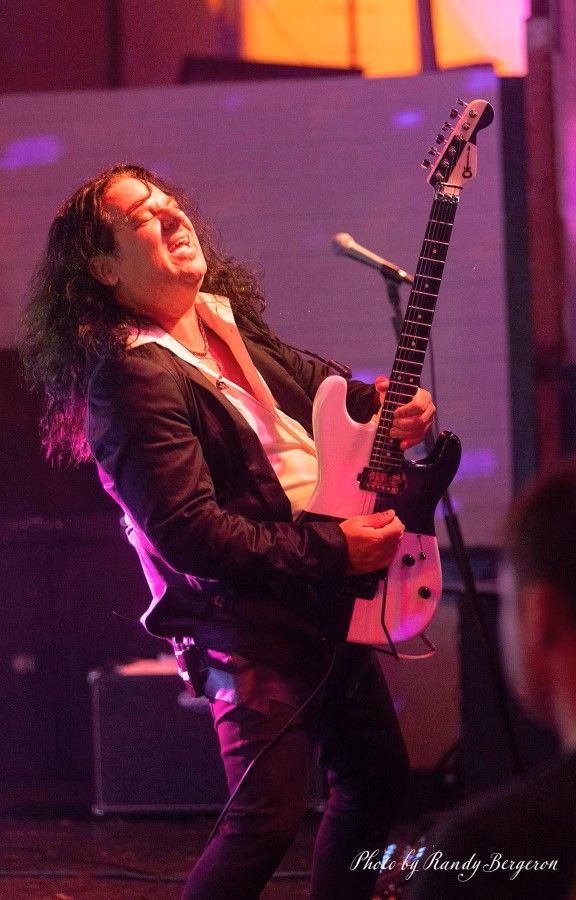 A man with long hair is playing a pink guitar in front of a microphone.