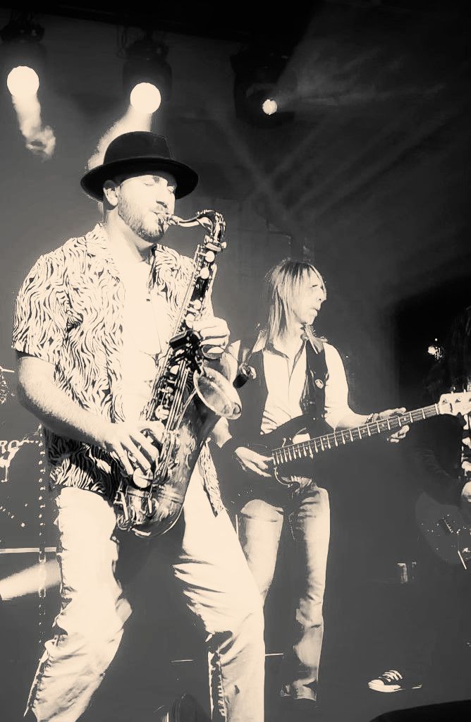 A man is playing a saxophone and a woman is playing a guitar on a stage.