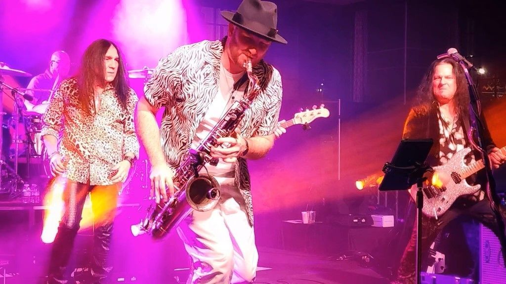 A man is playing a saxophone on stage while two women are dancing.