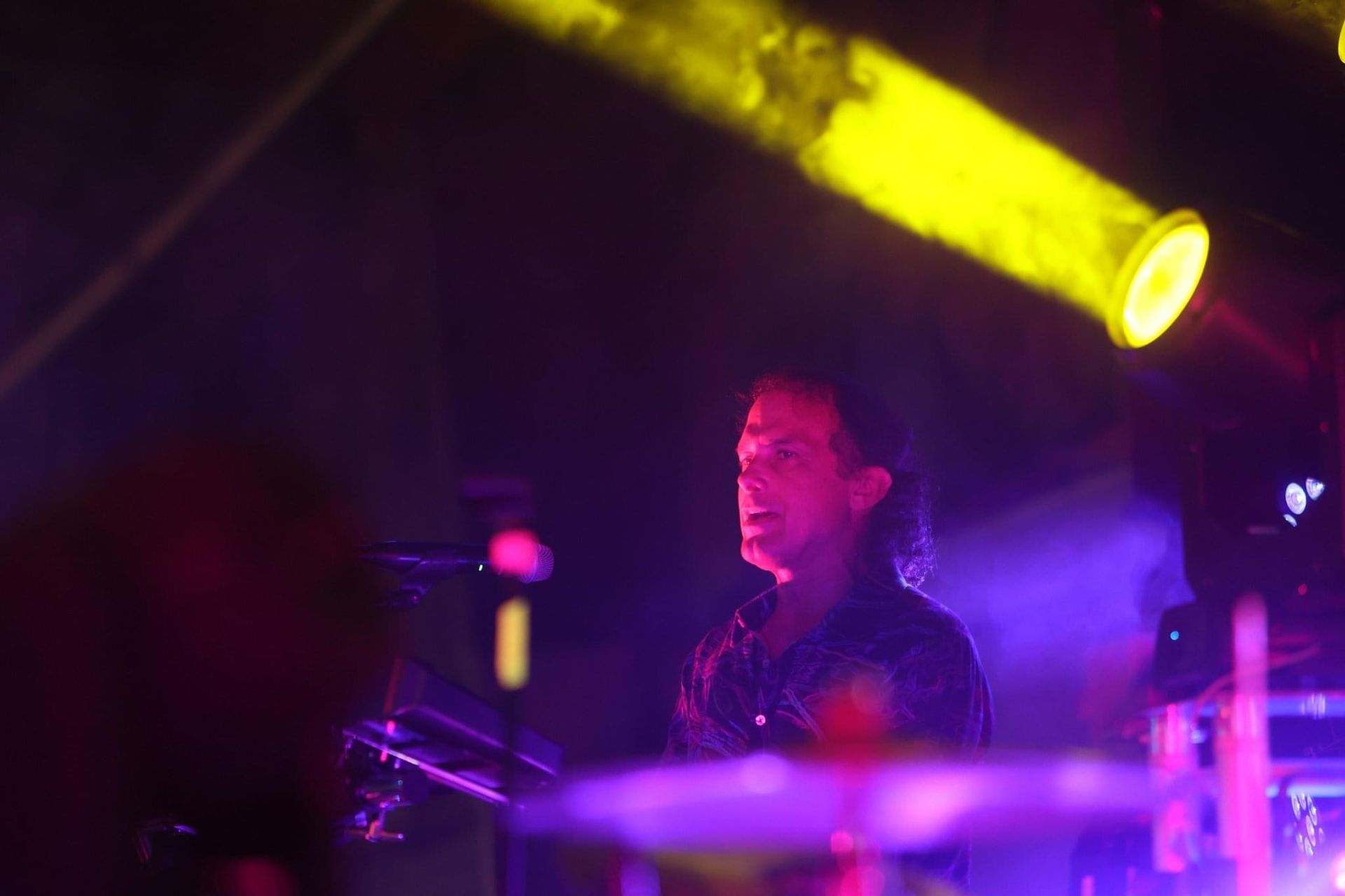 A man is playing drums on a stage in a dark room.