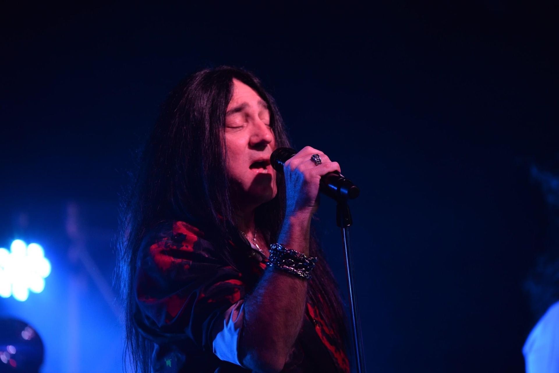 A man with long hair is singing into a microphone on a stage.