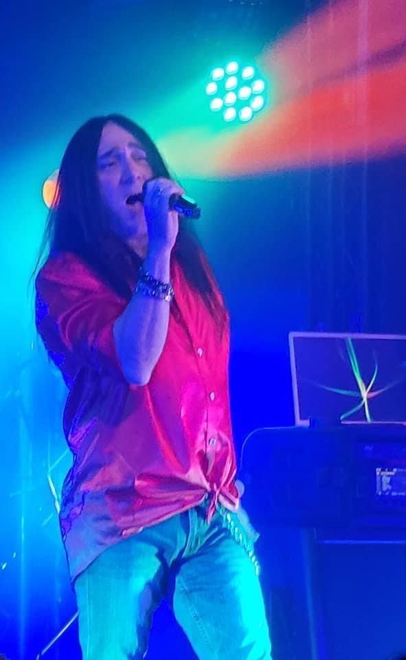 A man with long hair is singing into a microphone on a stage.