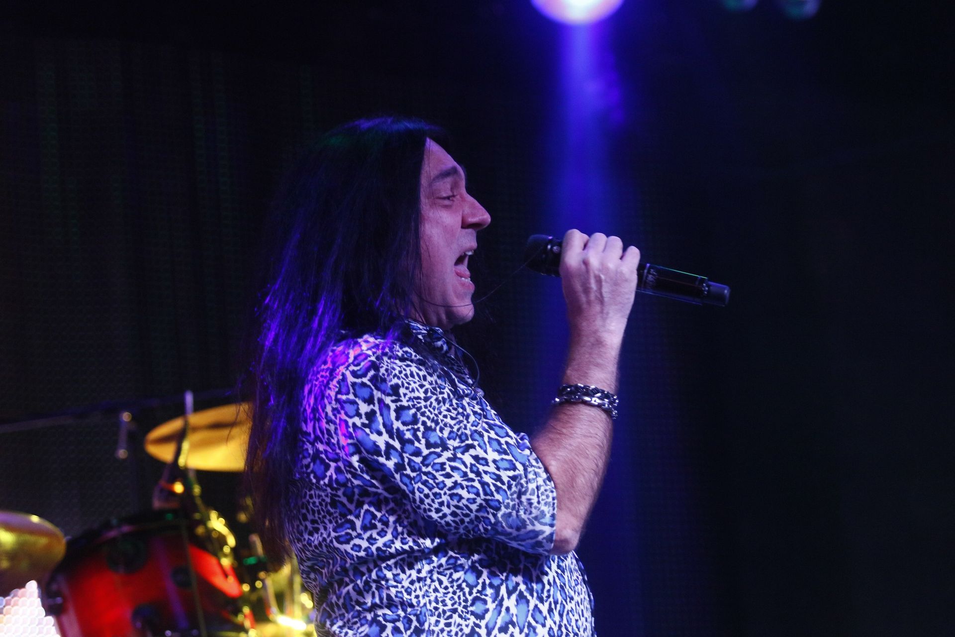 A man with long hair is singing into a microphone on a stage.