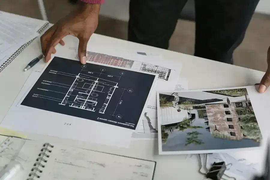 Hands reviewing architectural plans and a building render on a table