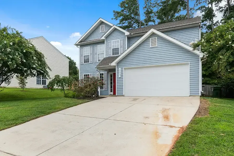 White two-story house with gray roof, dormer windows, and a covered front porch surrounded by trees