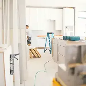 Bright kitchen under renovation with ladder, cabinets, and a person working near the back wall