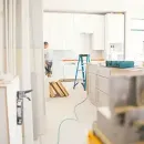Worker smoothing wet concrete with a trowel at a construction site, with blurred workers in the background