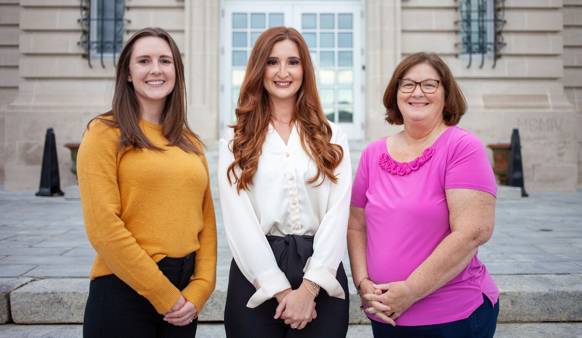 Three women are posing for a picture in front of a building.