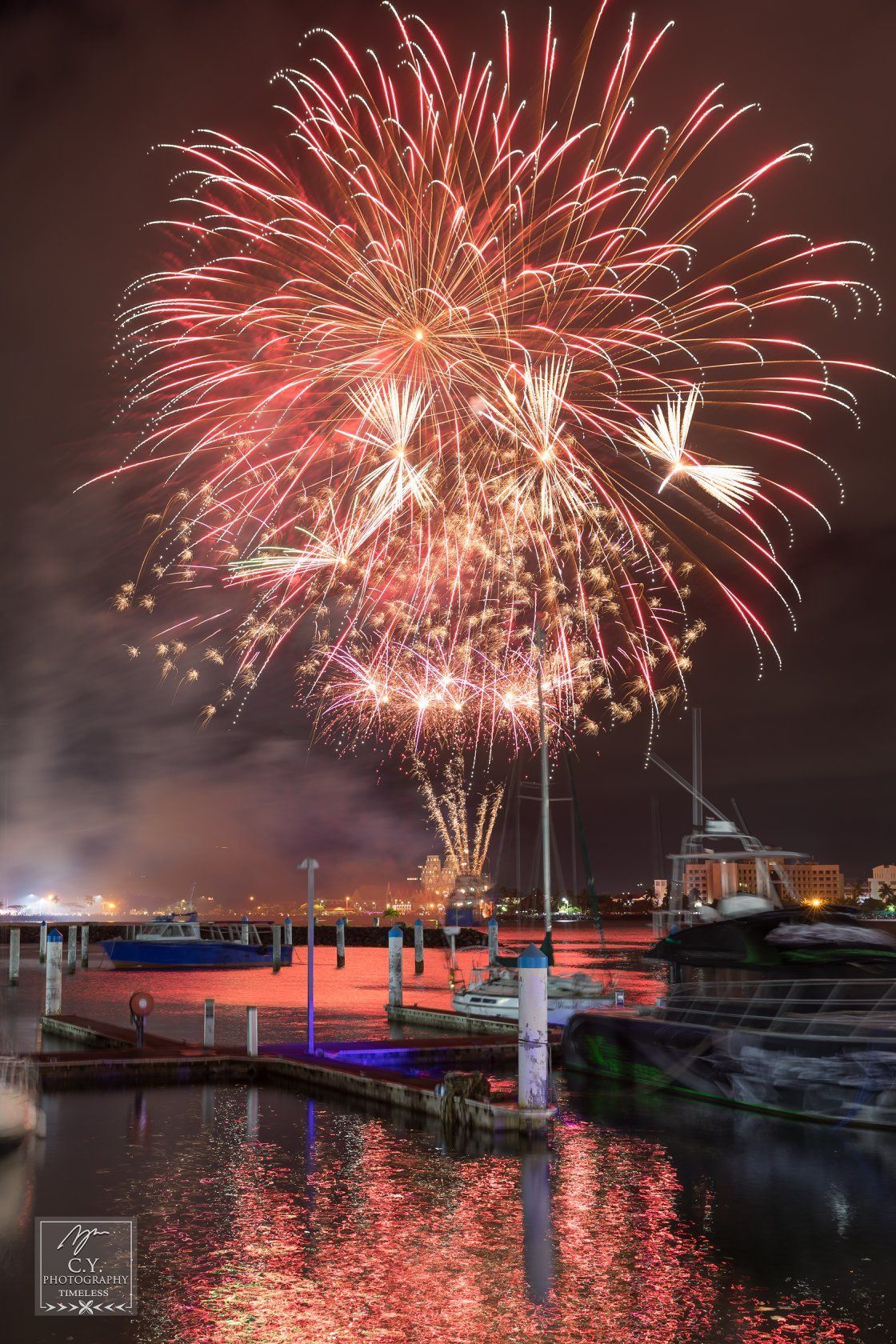 A fireworks display over a body of water with boats in the background