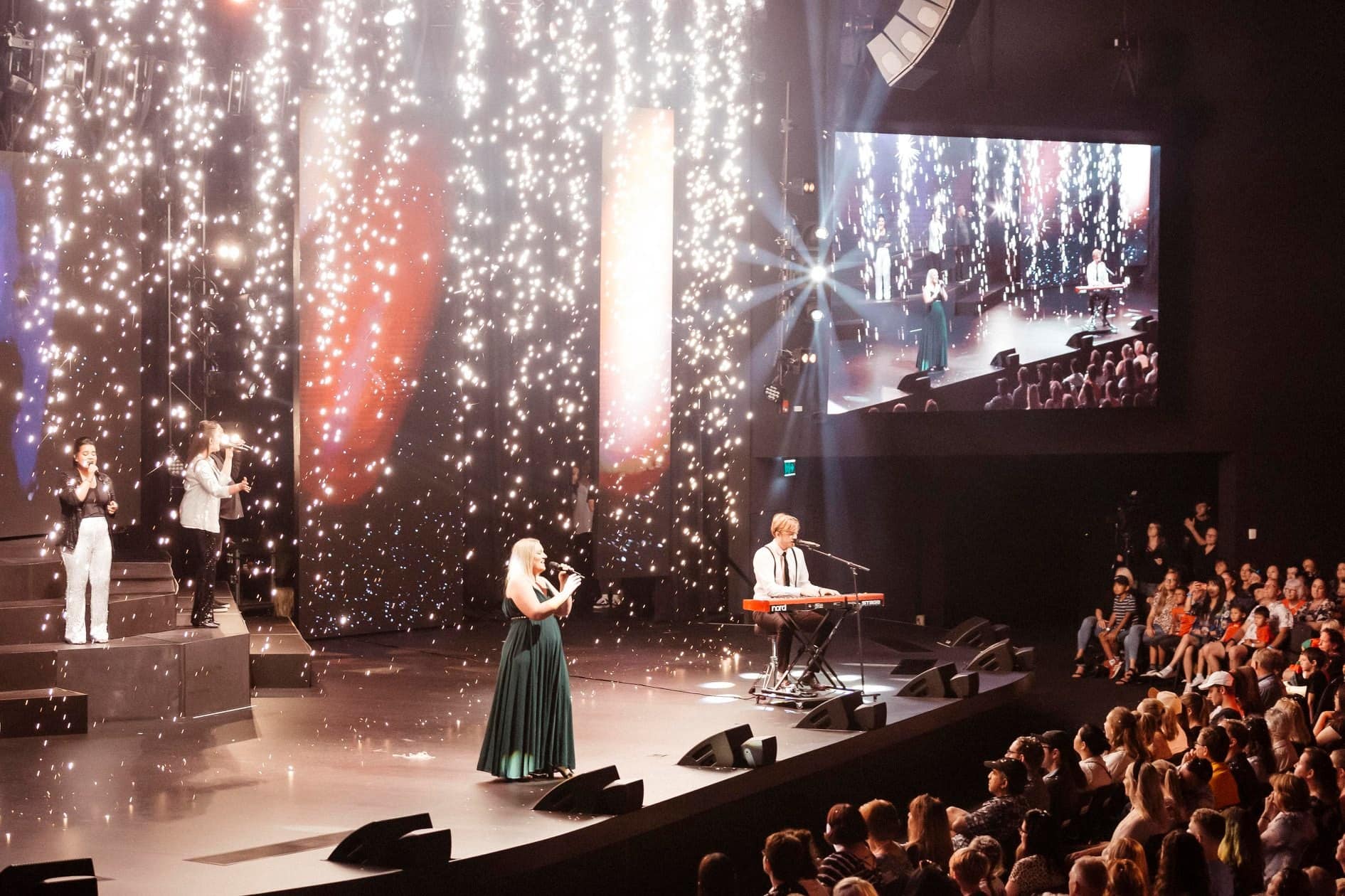 A group of people are standing on a stage in front of a crowd with falling spark effects