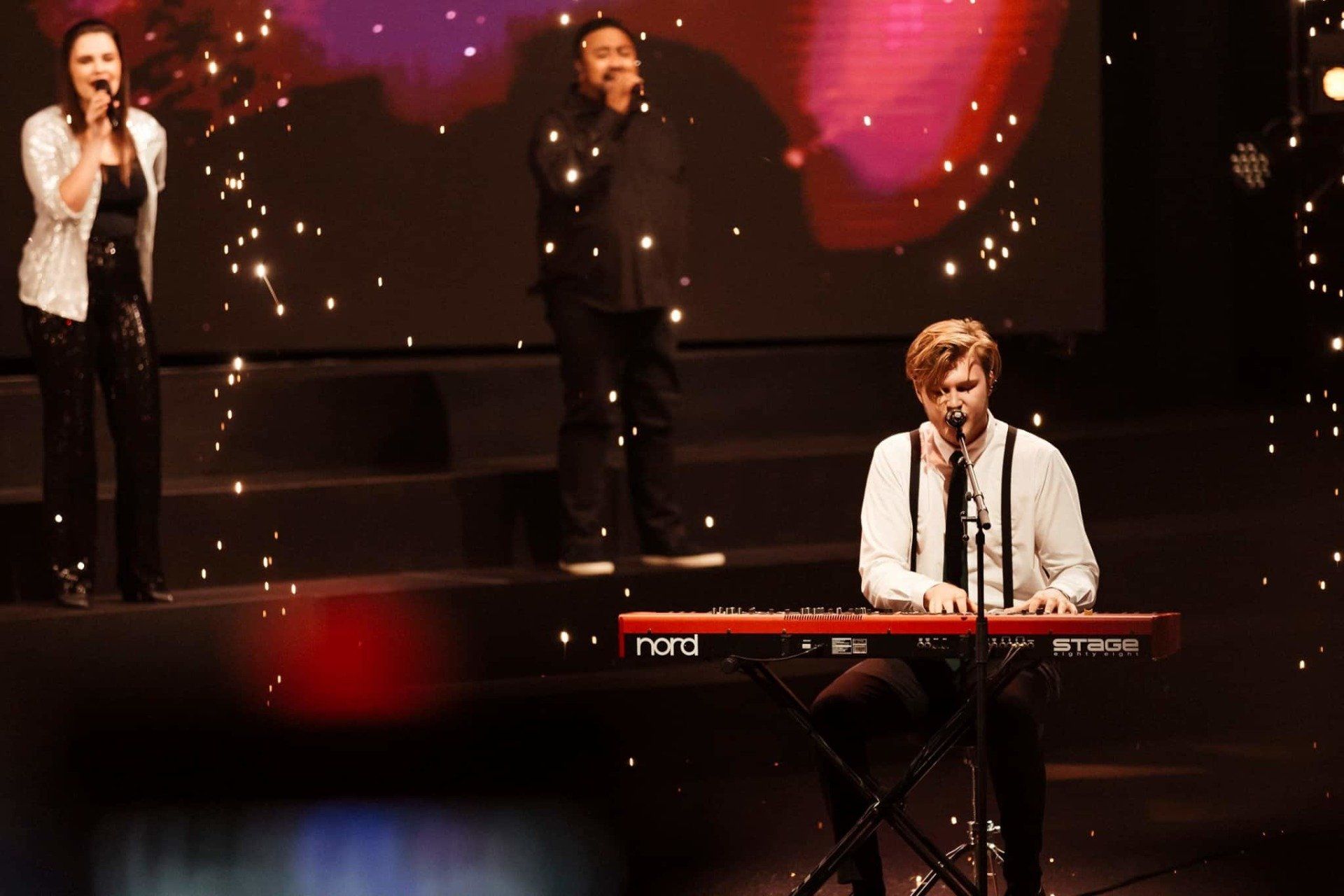 A group of people are singing and playing keyboards on a stage.