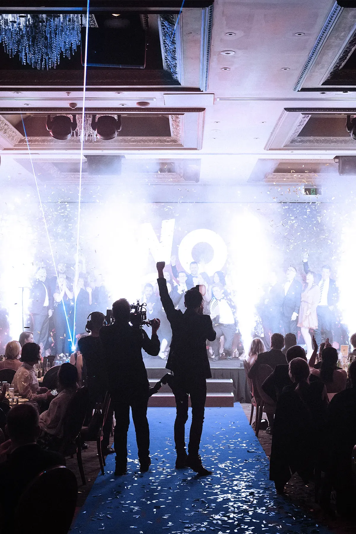 A group of people are standing in front of a stage with smoke coming out using sparks and indoor pyrotechnics