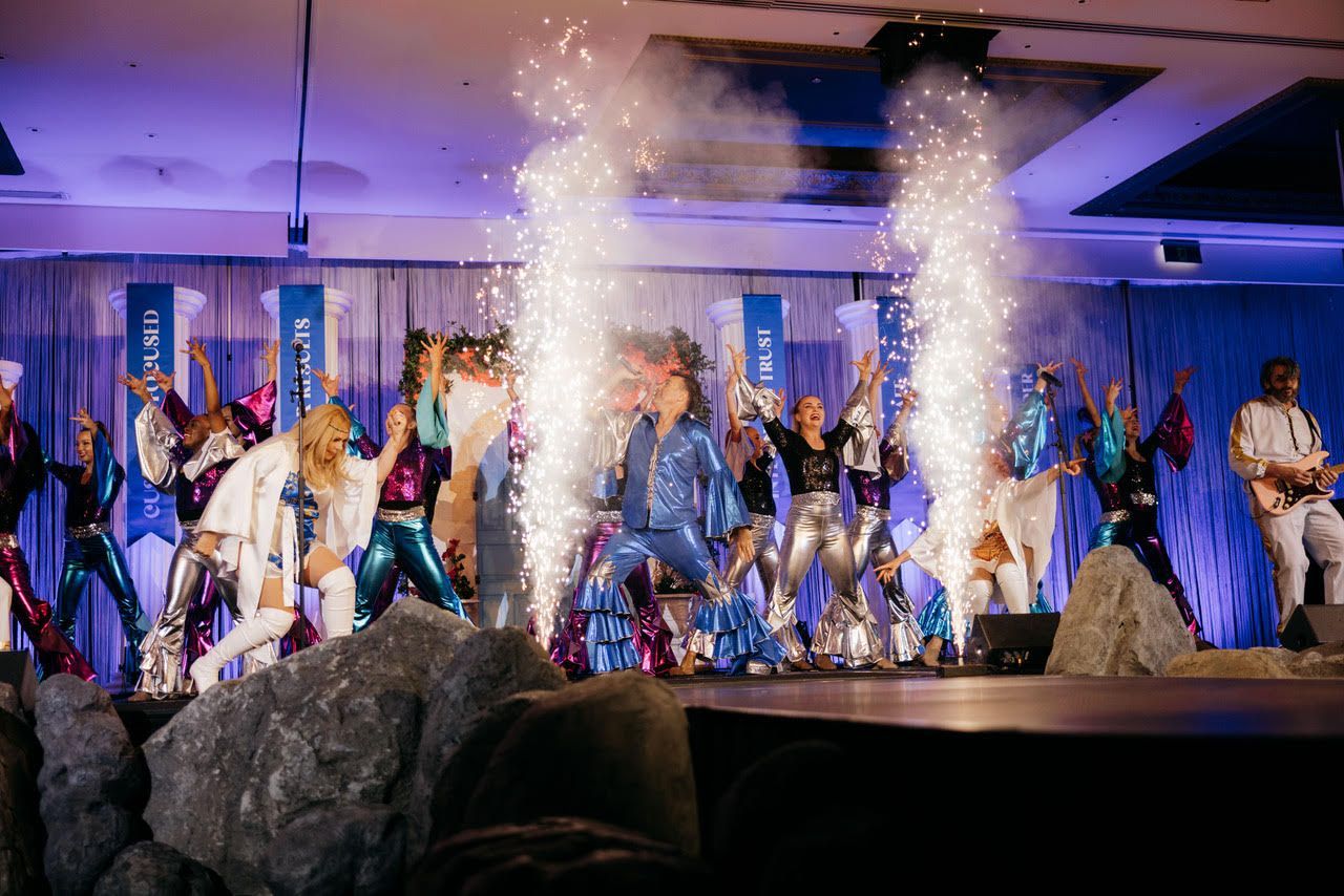A group of people are dancing on a stage with fireworks coming out of the ceiling.