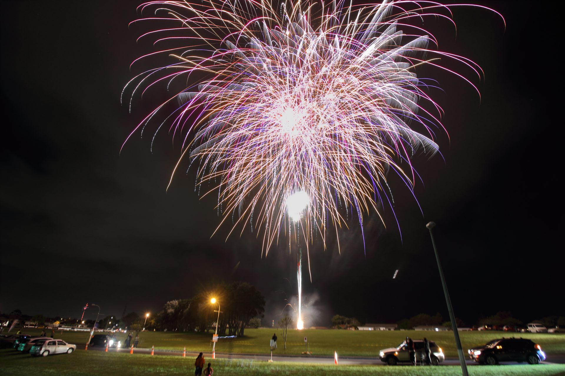 A fireworks display is taking place in a park at night for the Speedway fireworks 