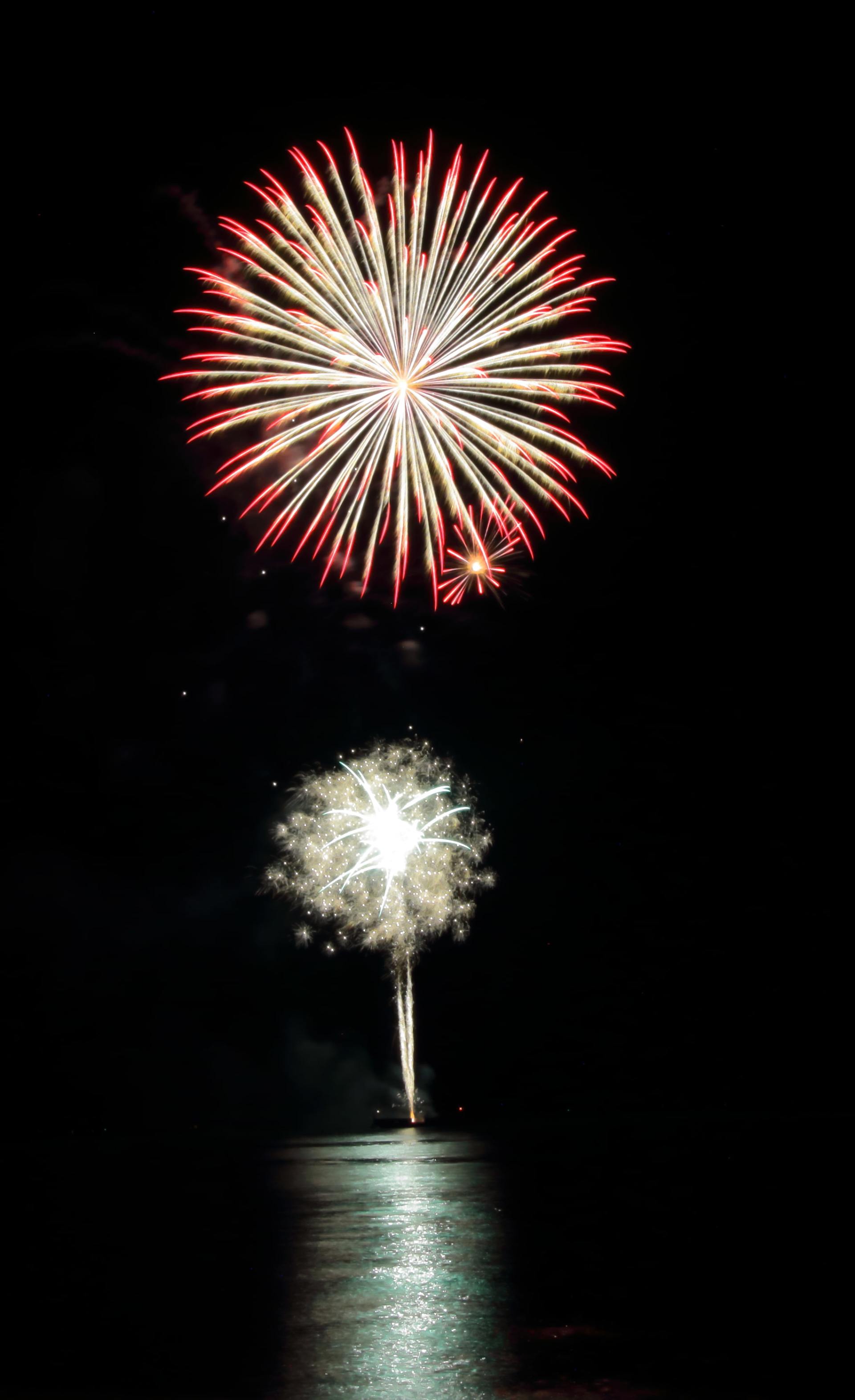 Two fireworks are displayed in the night sky over a body of water.
