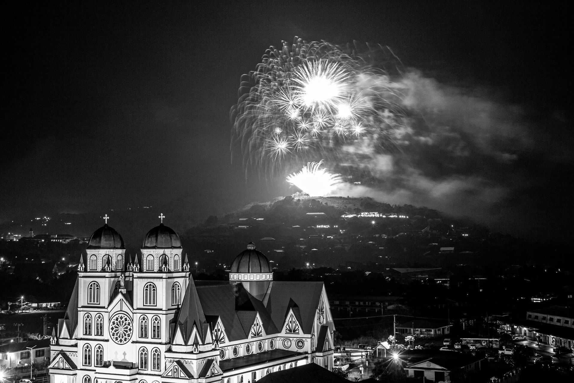 A black and white photo of fireworks over a church