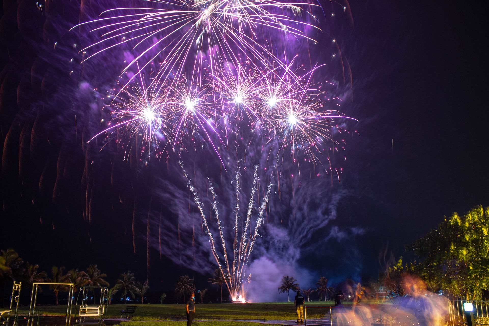 A person is standing in front of a fireworks display at night.