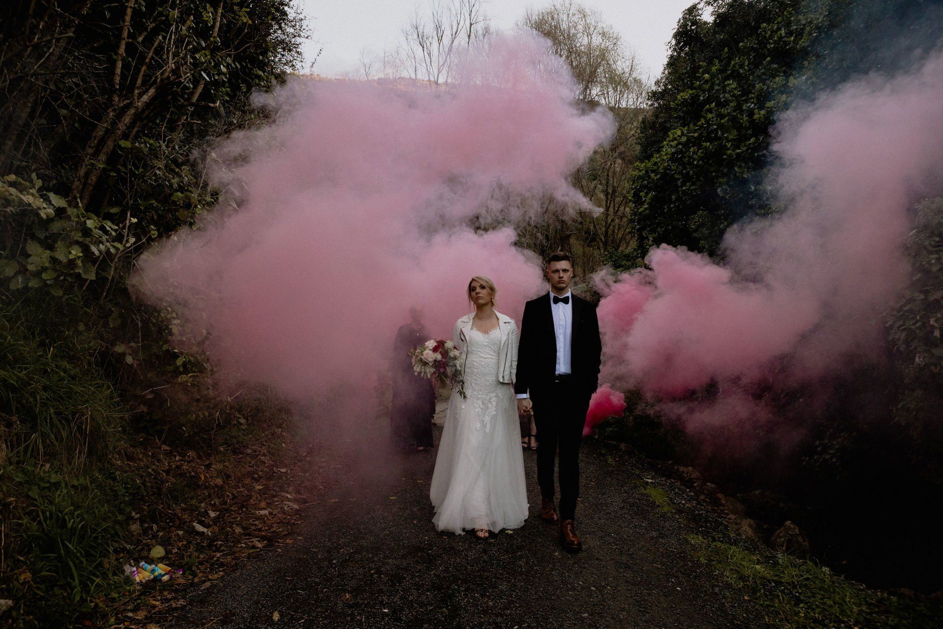 A bride and groom are standing next to each other in front of pink smoke.