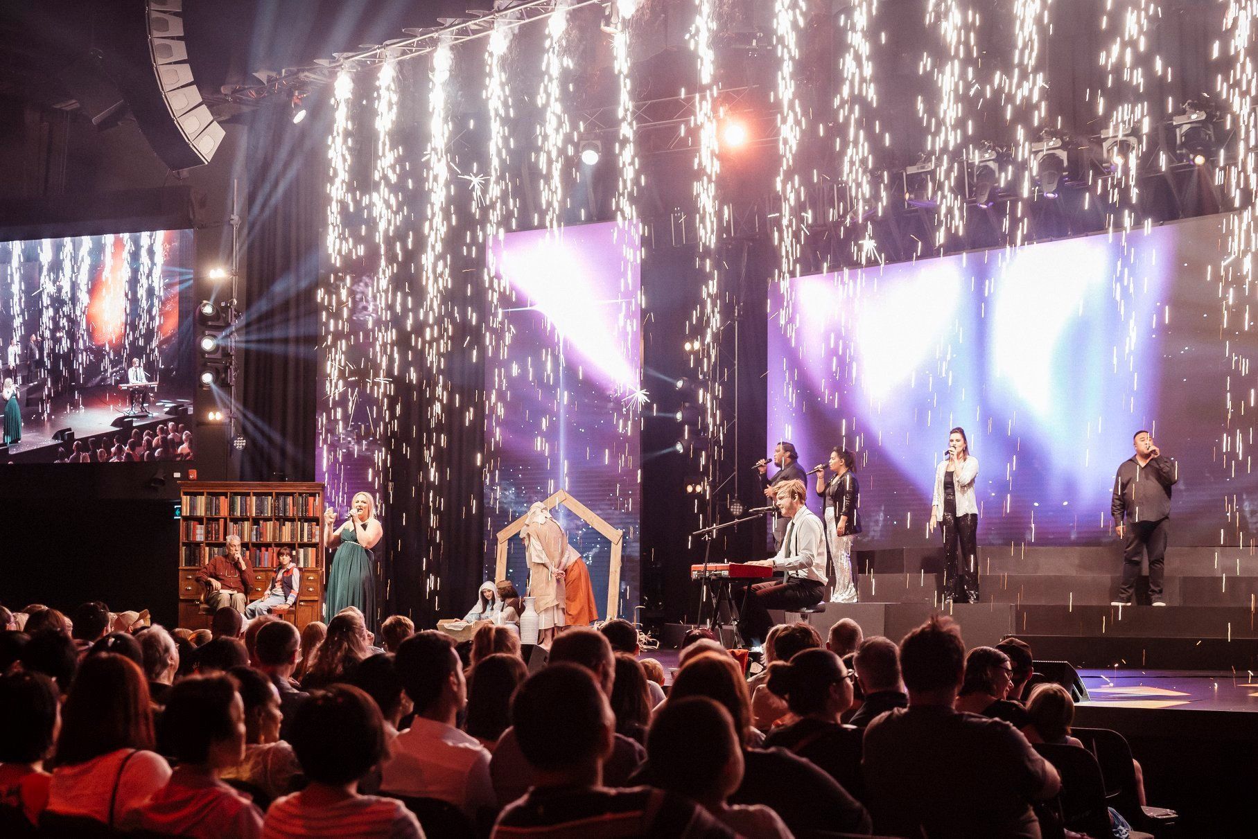 A group of people are sitting in front of a stage with fireworks coming out of it.