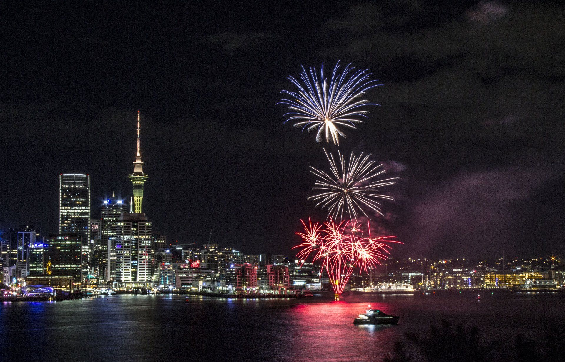 A fireworks display over a city with a boat in the foreground