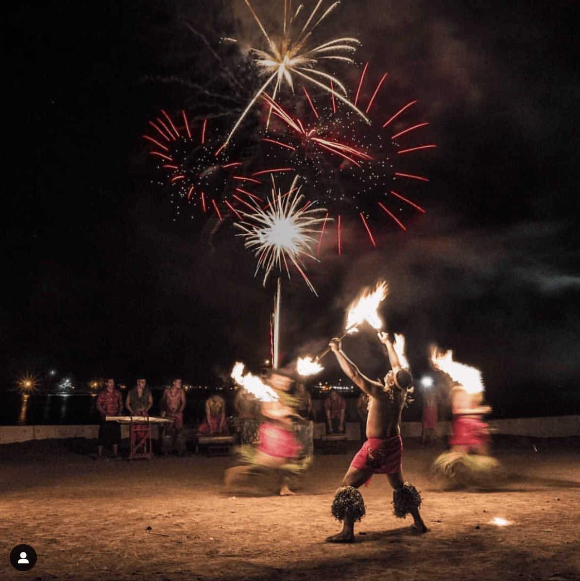 A man is holding a fire stick in front of fireworks.