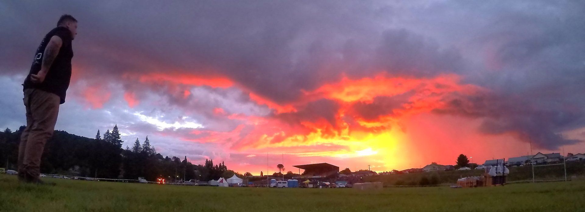 A man is standing in a field looking at a sunset waiting for the fireworks to shoot 