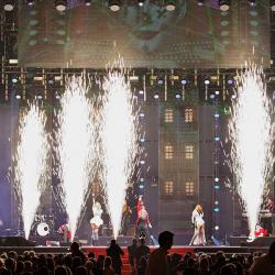 A group of people are standing in front of a stage with fireworks coming out of it.
