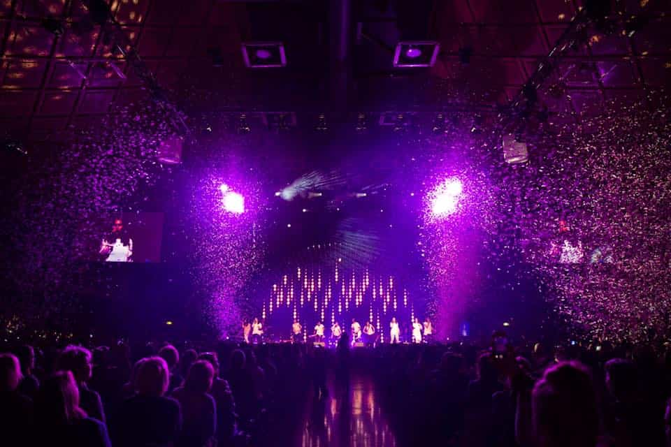 A crowd of people are sitting in front of a stage with purple lights.