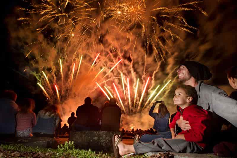A group of people are sitting on the ground watching fireworks.