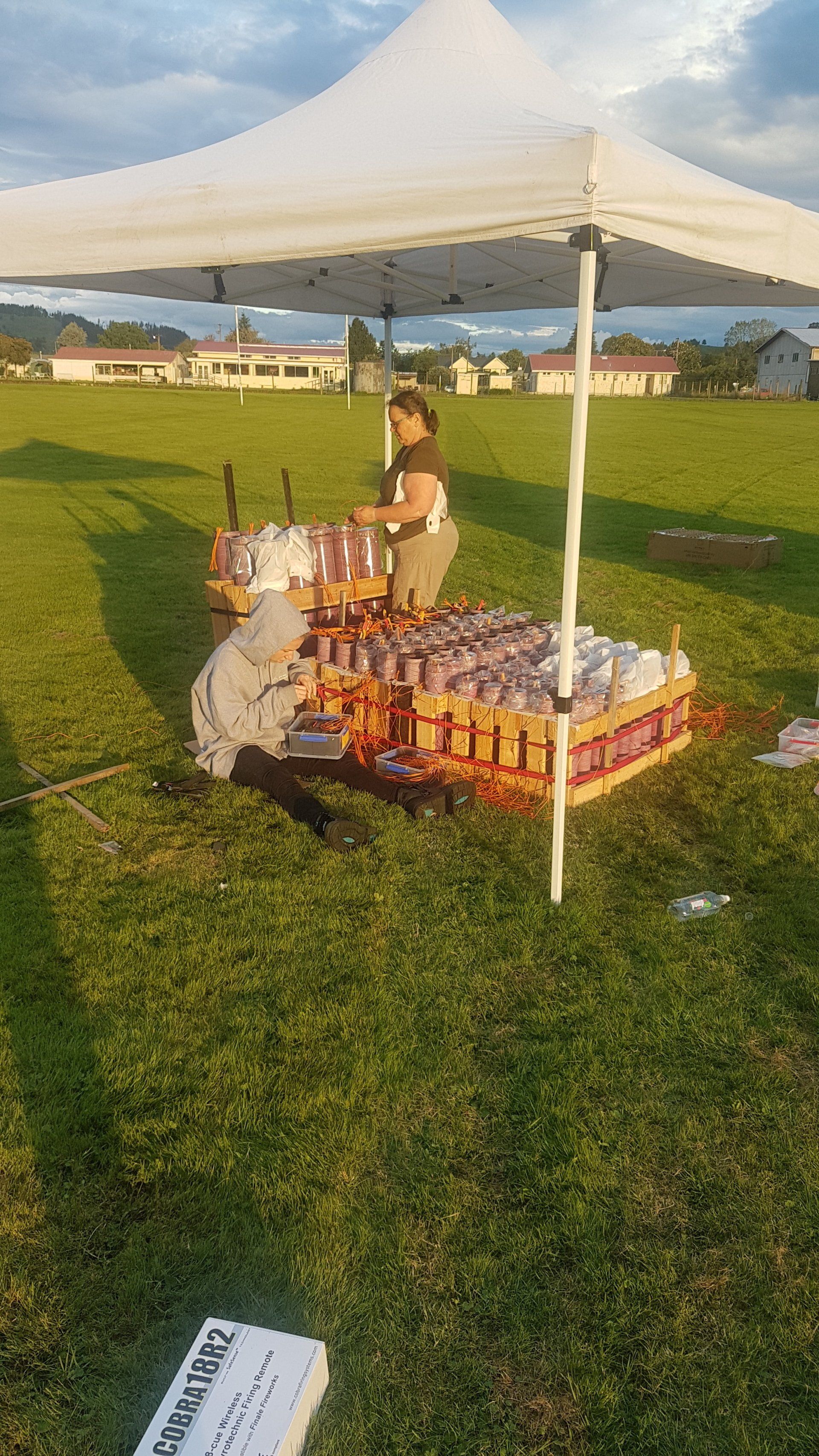 A woman is sitting under a white tent in a field. Setting up Fireworks for the Diwali Fireworks celebration