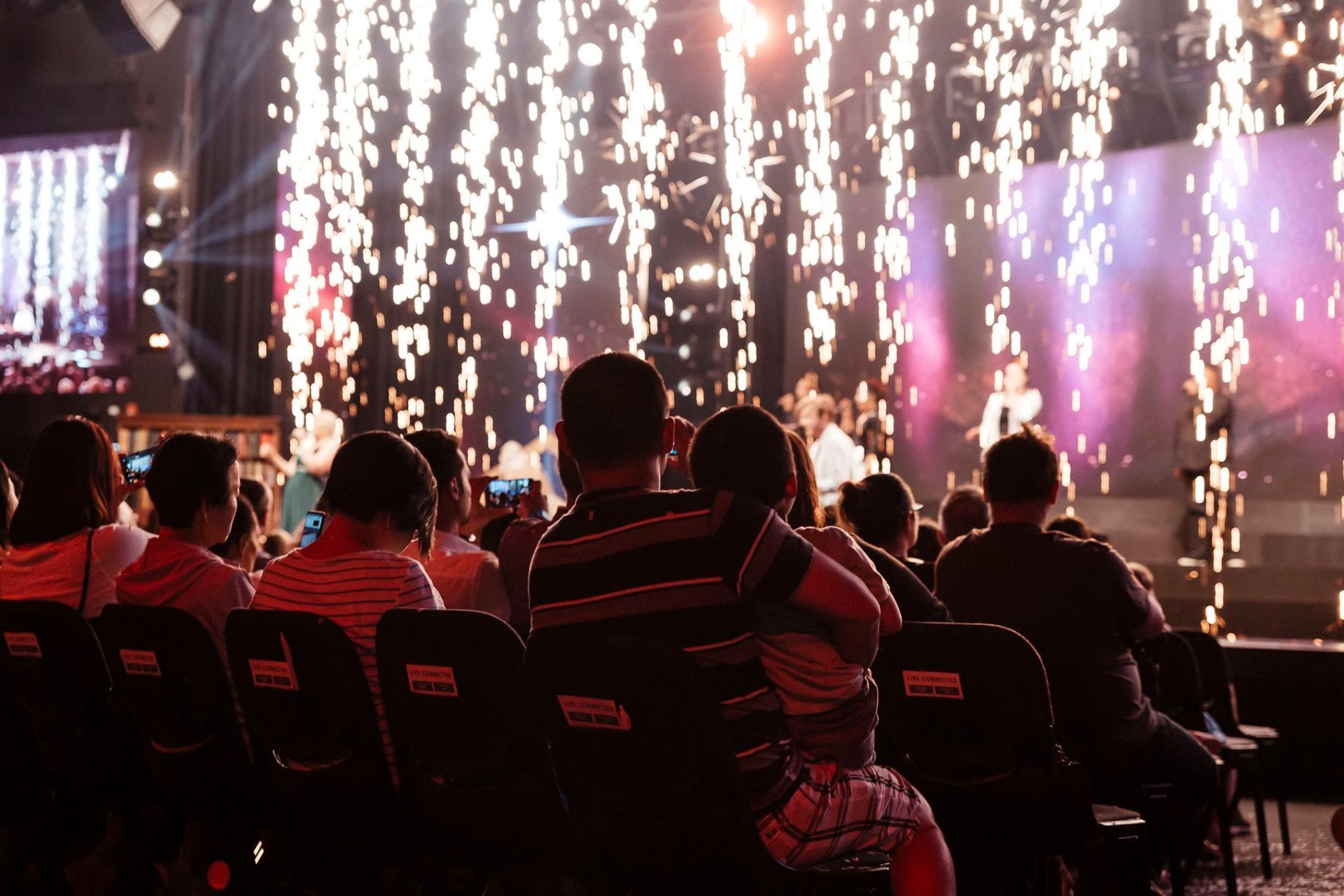 A group of people are sitting in chairs at a concert watching fireworks.