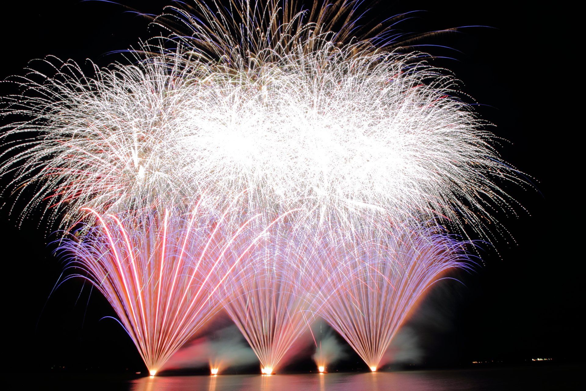 A bunch of fireworks are going off in the night sky over lake rotorua