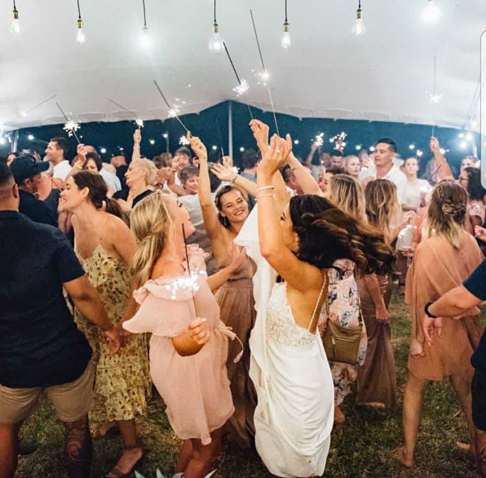 A group of people are dancing under a tent with sparklers.