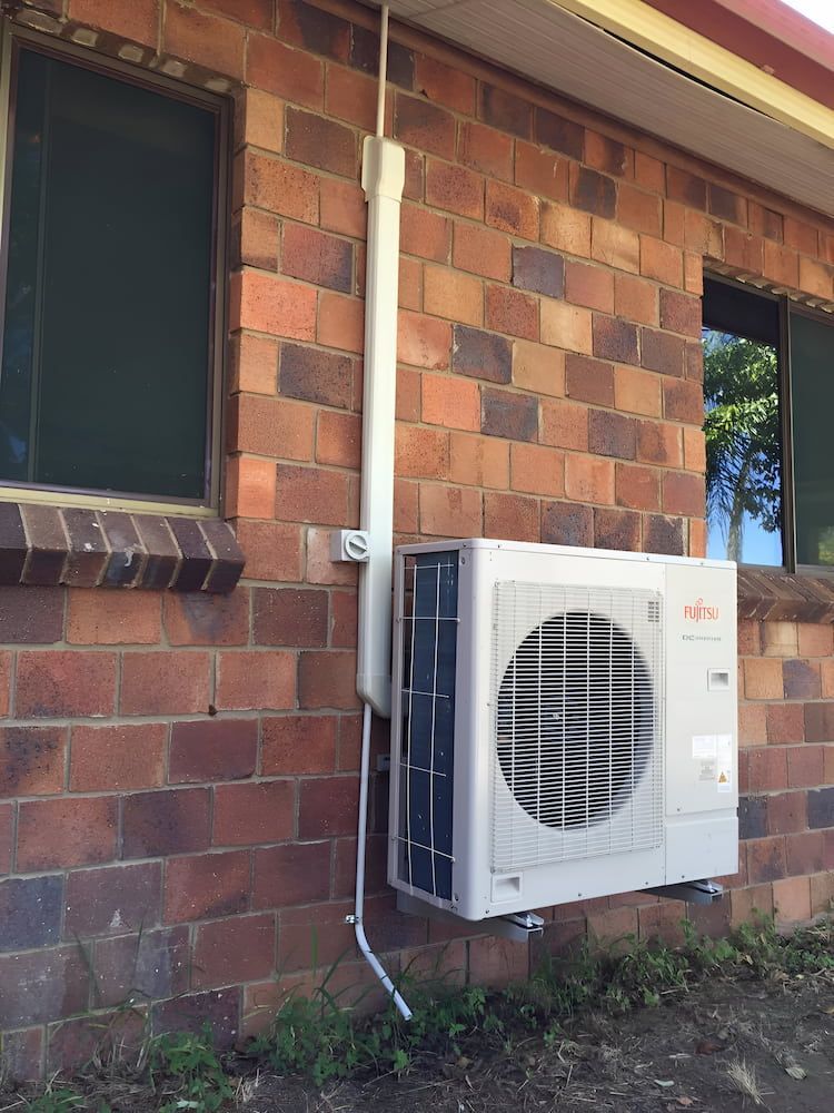 A White Air Conditioner Is Mounted On The Side Of A Brick Building — Levi's Electrics in Yeppoon, QLD