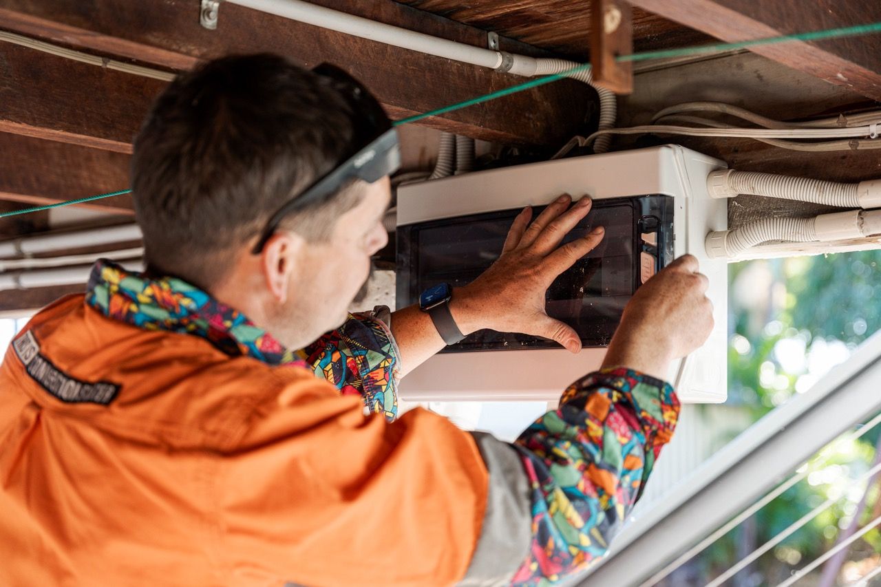 Tradesman Working On An Electrical Box Under A Building — Levi's Electrics in Nerimbera, QLD